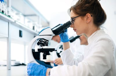 A female scientist wearing glasses, looking at a microscope