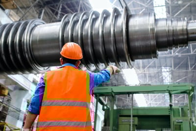 A man in an orange hard hat inspecting heavy machinery.