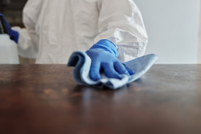 A person wearing blue medical gloves swiping a wooden table.