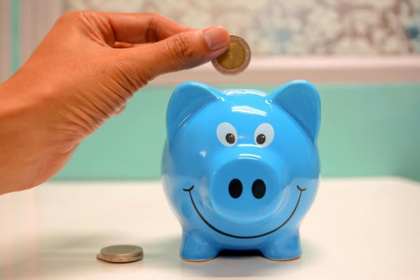 A woman putting a coin in a blue piggy bank