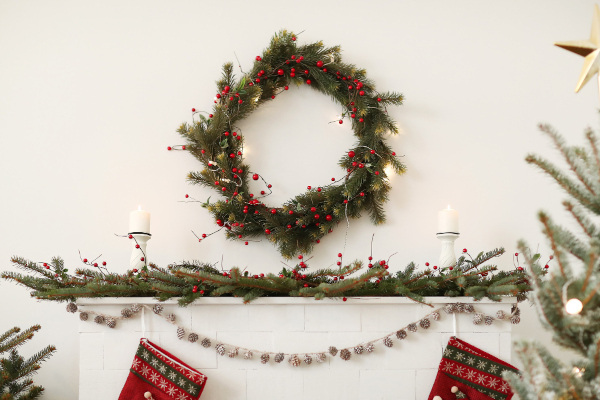 A wreath and some garlands hanging on a white fireplace