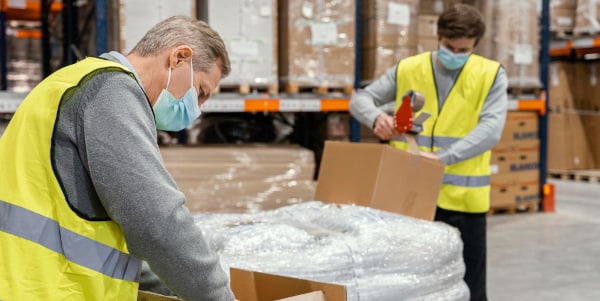 Two warehouse workers checking packed boxes in a wareshouse.